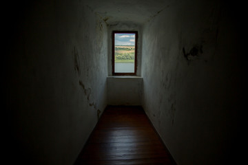 A window in the ancient castle wall, a view of a sunny day of summer forest, a hill, and a river.