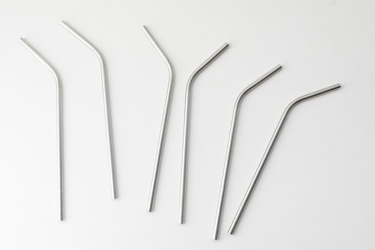 High angle view of six metal drinking straws scattered on white background