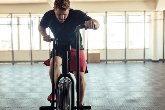 Fit young man using air bike for cardio workout at gym
