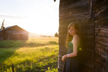 Young girl leaning on a barn with sunflare looking left