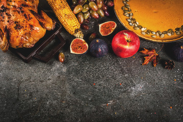 Thanksgiving Day food. Roasted whole chicken or turkey with autumn vegetables and fruits: corn, pumpkin, pumpkin pie, figs, apples, on dark grey background, top view  copy space