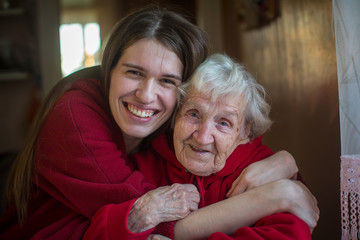 An elderly woman in an embrace with his adult daughter. Positive portrait in the house.