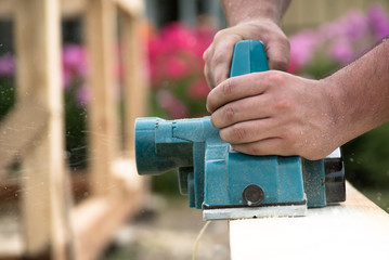 Close up hands of carpenter working with electric planer on wooden plank