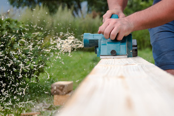 Close up hands of carpenter working with electric planer on wooden plank