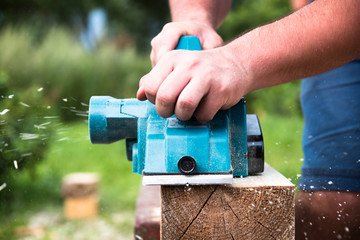 Close up hands of carpenter working with electric planer on wooden plank