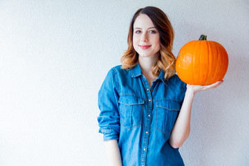 Redhead woman in jeans clothes holding orange autumn pumpkin