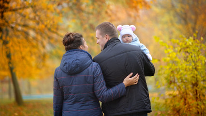 happy family walks in a beautiful autumn park, father holds a baby in his arms and smiles