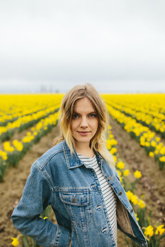 Portrait Of Young Blonde Woman Standing In Field Of Yellow Daffodils