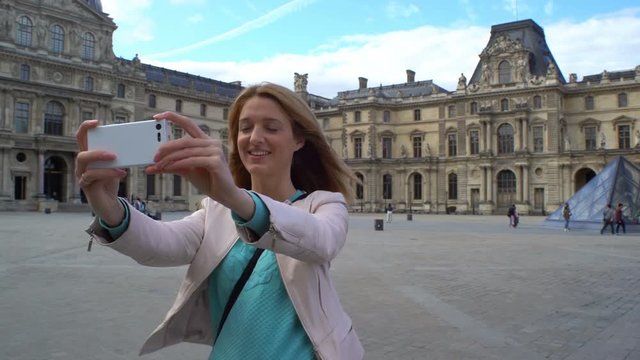 Young Happy Woman Making Selfie uses a Smartphone in Paris, the Louvre