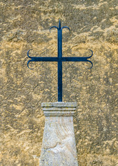 Ancient iron cross in stone base in front of a wall