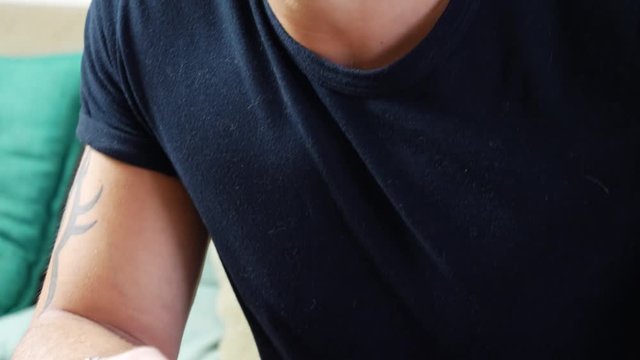 Attractive young man using joystick or joypad for videogames, sitting on couch at home in his living room, staring at TV screen