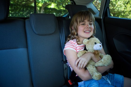 Teenage girl with teddy bear sitting in the back seat of car