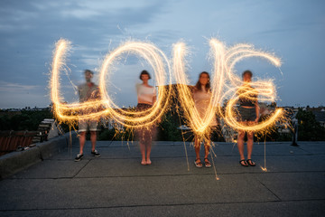 Four people writing the word 'love' with sparklers.
