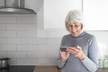 happy senior woman in her kitchen using an electronic mobile device