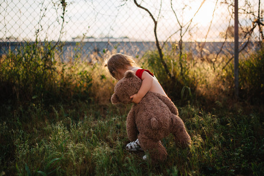 Small toddler child walking around with a teddy bear in red suspenders.