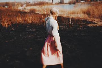 Blonde girl walks on the burned field