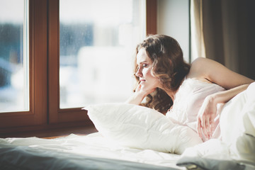 Woman lying in bed at early morning near window.