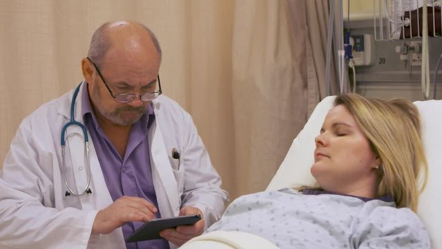 Doctor gets patient information from his tablet computer, bedside with a patient at a hospital.