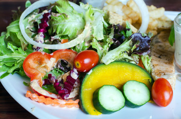 fish steak, grilled salmon and fresh vegetable salad, french fries and sauce on a white plate