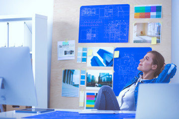 Two young woman standing near desk with instruments, plan and laptop.
