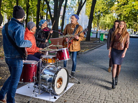 Festival music band. Friends playing on percussion instruments in autumn city park. Fountain and trees in background. People like street music.