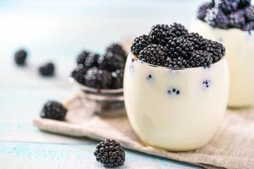 Fototapeta na wymiar Clear jar of yogurt with blackberry over on wooden background