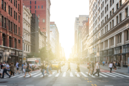 Groups of people walking across a busy crosswalk intersection in New York City with the glow of the sun in the background