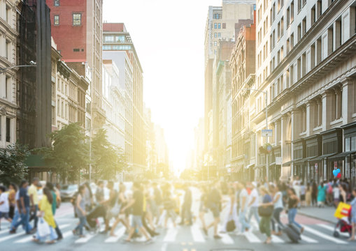 Crowds of colorful diverse people walking across a busy intersection in New York City with the light of the sun glowing in the background