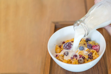 fresh milk on the white cup, cornflakes cereal, strawberry, blackberry and milk in a white bowl, selective focus.