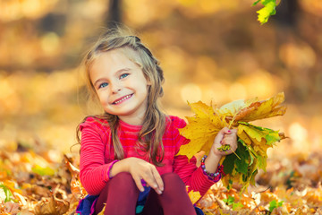 Naklejka na ściany i meble Happy little girl with autumn leaves in the park