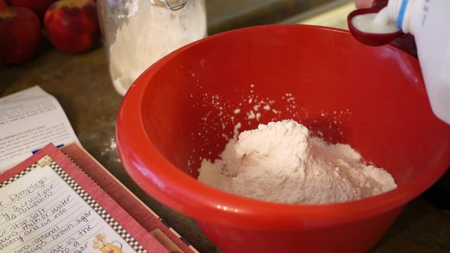 Woman adding milk to flour in red bowl in kitchen