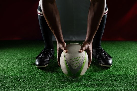Low section of rugby player holding ball while standing against - Powered by Adobe