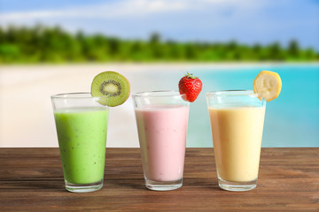 Glasses of different protein shakes and landscape on background