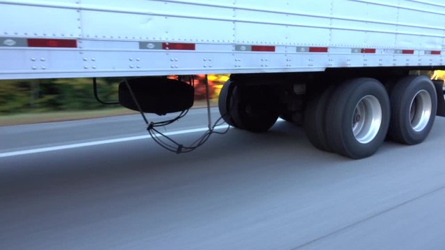 CLOSE UP: White freight semi truck passing by on highway. Detail of truck's wheels and tires rolling on dry freeway asphalt. 18 wheeler transporting cargo, tyres spinning fast along the motorway
