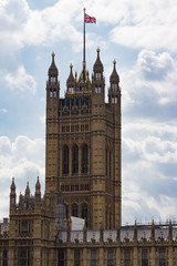 Close Up Vertical shot of the Victoria Tower or the King's tower of the Palace of Westminster and Houses of Parliament with the British flag waving in a cloudy sky.