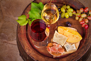 Red and white wine with cheese, prosciutto and grape on old wine barrel in cellar. Food and drinks concept. View from above, top, horizontal