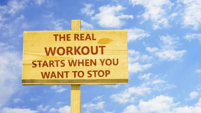 The real workout starts when you want to stop. Words on a wooden sign against time lapse clouds in the blue sky. 