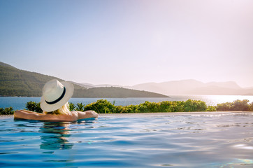 A girl in a hat admires the sunset from the pool.