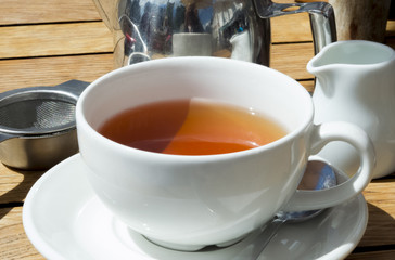 Cup of tea on wooden table with mug, pot and strainer