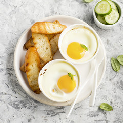 Breakfast for two. Eggs baked in the oven in ceramic portioned forms with toasted bread and slices of fresh cucumber. Top View.