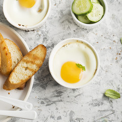 Breakfast for two. Eggs baked in the oven in ceramic portioned forms with toasted bread and slices of fresh cucumber. Top View.