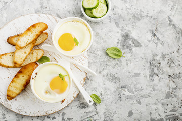 Breakfast for two. Eggs baked in the oven in ceramic portioned forms with toasted bread and slices of fresh cucumber. Top View.