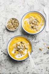 Pumpkin and apple cider soup with a topping of crispy toasted pumpkin seeds, sunflower seeds and oat flakes in a serving bowl on a light background. Top View.