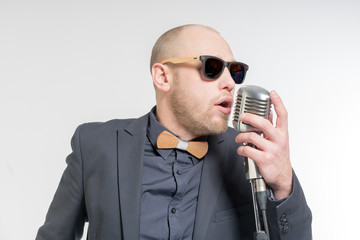 Naklejka premium Unshaven bald man in a gray suit and sunglasses holding a microphone and singing. Toned