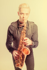 Naklejka premium Elegant blond man dressed in black, playing the saxophone. Toned