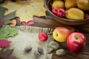 pears and red apples in clay plate, scattered with fallen leaves on wooden table