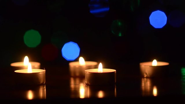 burning candles on a table in a dark room, festive decoration of the room, blinking colorful bokeh heart blue red green