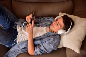 Teen lying face up on couch consuming multimedia top view
