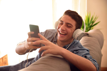 Teenager laughing with smartphone leaning on the back of couch