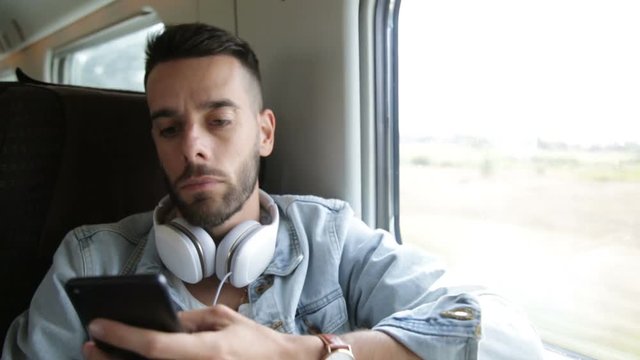 Ragazzo sta viaggiando su un treno mentre ascolta musica dalle cuffie e usa lo smart phone.